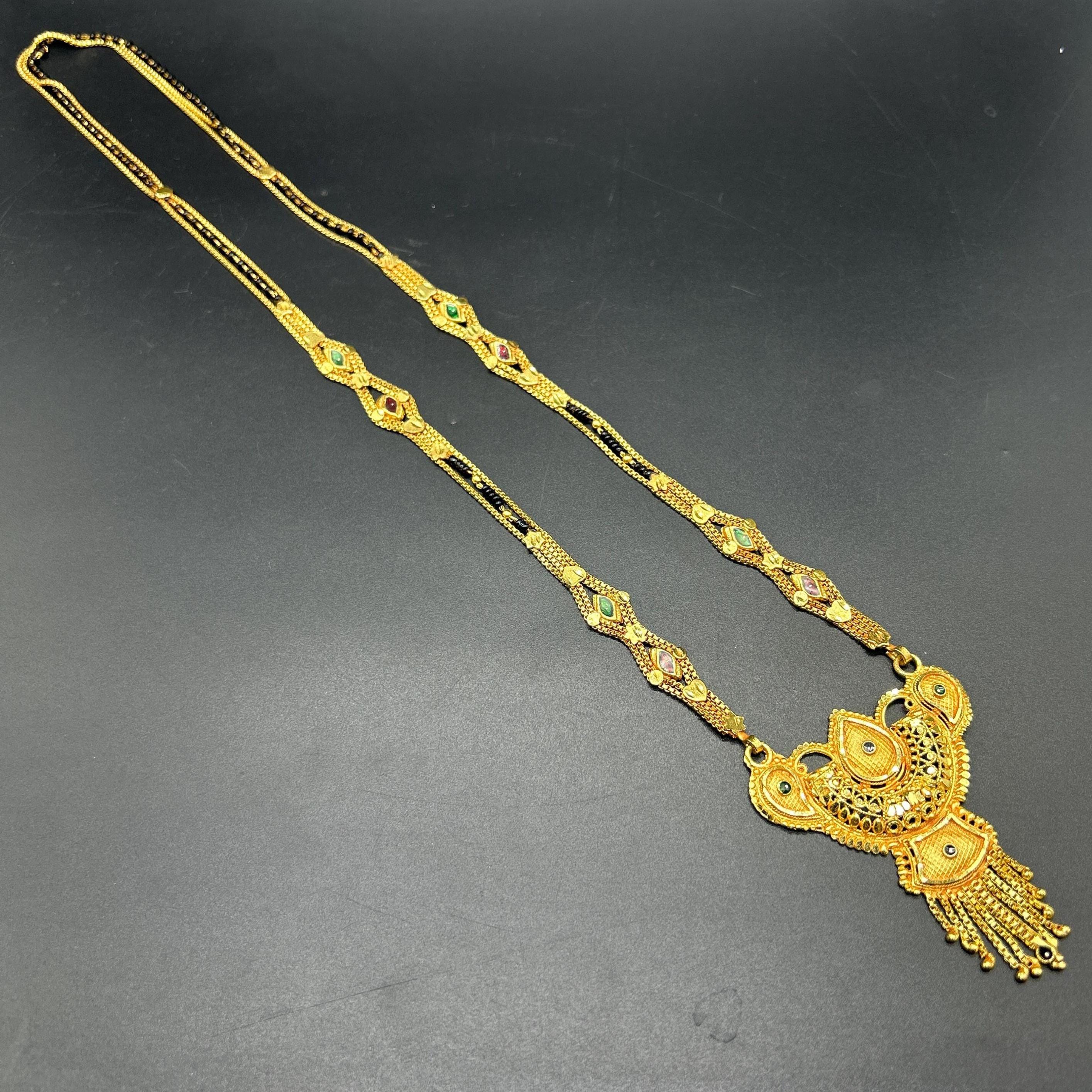 Gold-plated black beaded long mangalsutra, has a stylized centerpiece with textured details