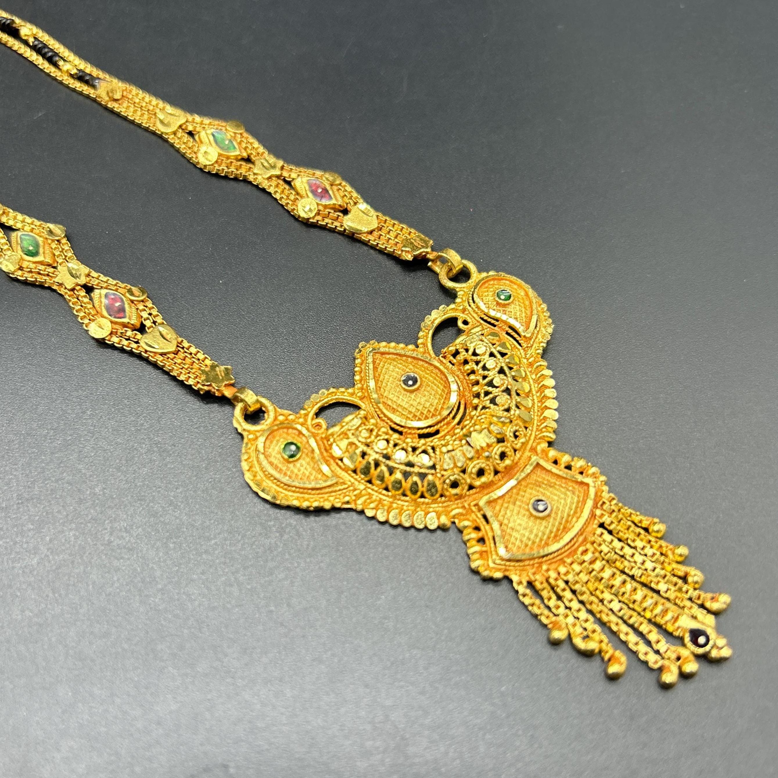 Gold-plated black beaded long mangalsutra, has a stylized centerpiece with textured details